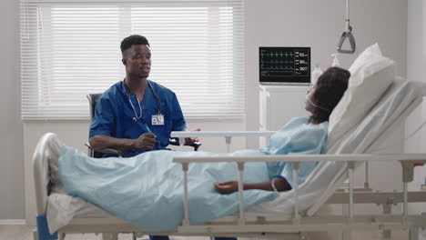 Im-Krankenhaus-Untersucht-Ein-Afrikanisch-amerikanischer-Schöner-Arzt-Eine-Patientin,-Die-Auf-Dem-Krankenhausbett-Liegt-Und-Mit-Ihr-Spricht,-Beide-Lächeln